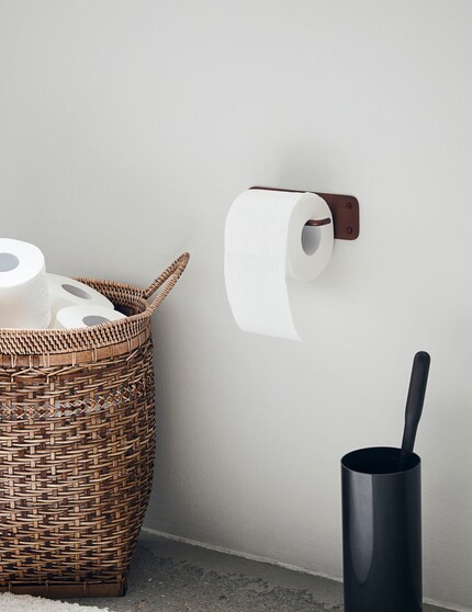 The open toilet paper holder is functional, and its reddish-brown colour brightens up the wall.