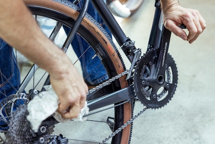 Elia pushing the saddle into his stomach, applying tension to the chain via the pedal and rubbing it clean.